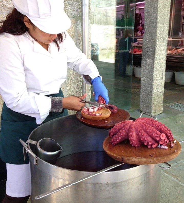 Plating the octopus. Small wooden plates are used to serve, and large wooden platters hold the octopus. The hooks used by the cooks are holding up the large platter with the cooked octopus.