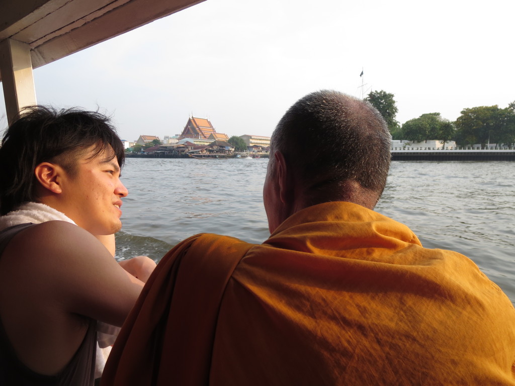 Monk and Man Chat on Chao Phraya Ferry with Wat Kalayanamitr in the Background