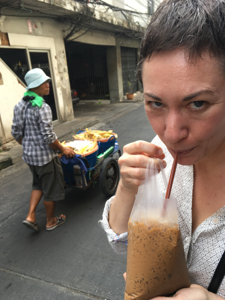 Alison sips iced coffee from a plastic bag in Bangkok.