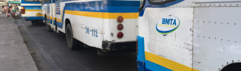 Buses painted blue, white, and yellow await commuters at the Memorial Bridge ferry terminal in Bangkok.