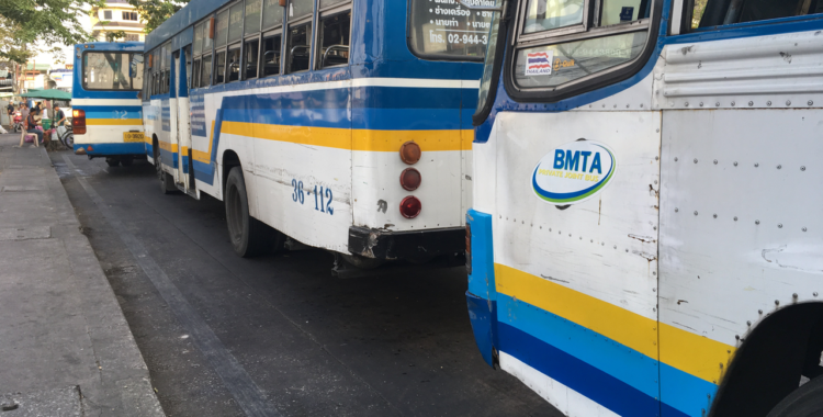Buses painted blue, white, and yellow await commuters at the Memorial Bridge ferry terminal in Bangkok.